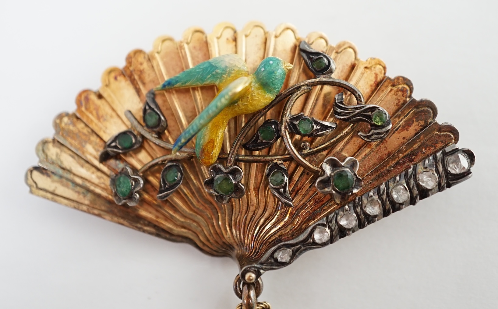 A gold (test as 15ct), emerald, rose cut diamond and enamel set brooch, modelled as a fan with applied parrot on a branch